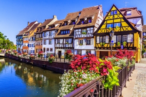 Fachwerkhäuser an einem Kanal mit Blumen geschmückter Brücke.
