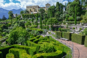 Historischer Garten mit Schloss und Labyrinth aus Hecken im Hintergrund.