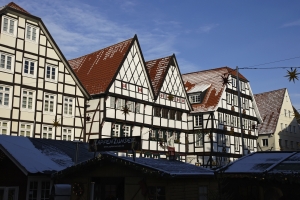 Fachwerkhäuser mit schneebedeckten Dächern unter blauem Himmel.