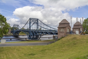 Eine blaue Stahlbrücke überquert einen Fluss unter bewölktem Himmel.