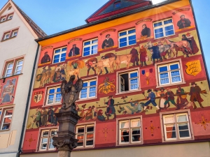Bunt bemalte Fassade eines historischen Gebäudes mit Figuren und Szenen.