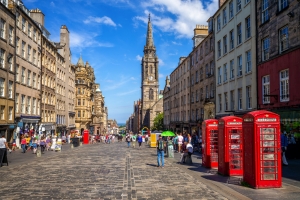 Historische Straße mit roten Telefonzellen und Menschen bei sonnigem Wetter.