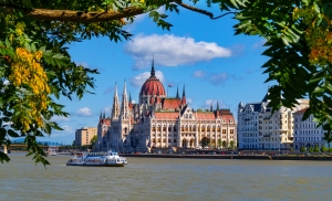 Parlamentsgebäude von Budapest, Ungarn, am Ufer der Donau, umrahmt von Bäumen im Vordergrund.