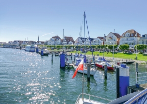 Hafen mit Segelbooten und Häusern im Hintergrund bei sonnigem Wetter.