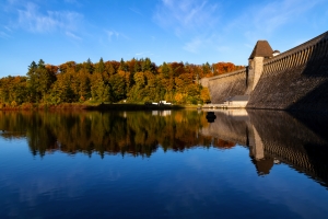 Möhnesee-Talsperre in Nordrhein-Westfalen im Herbst, Wasser spiegelt Bäume und Staumauer bei klarem Himmel.