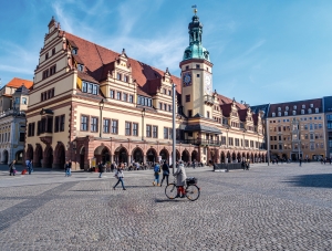 Historisches Gebäude mit Turm auf großem, belebtem Platz bei blauem Himmel.