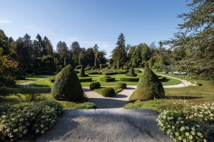 Französischer Garten mit symmetrischen Hecken und Bäumen bei klarem Himmel.