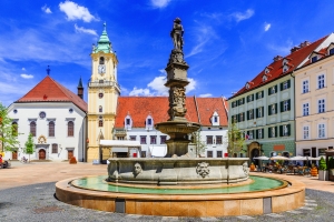 Historischer Platz mit Brunnen und Gebäuden unter klarem Himmel.