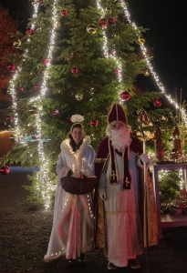 Zwei festlich gekleidete Personen vor einem geschmückten Weihnachtsbaum bei Nacht.