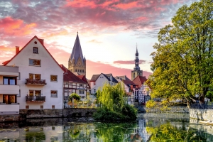 Ein Blick auf die Altstadt von Soest in Nordrhein-Westfalen mit Fachwerkhäusern am Wasser und einer Kirche im Hintergrund unter einem farbenfrohen Himmel.