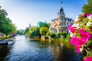 Ein Kanal in Amsterdam, Niederlande, mit Giebelfassaden und Blumen im Vordergrund.
