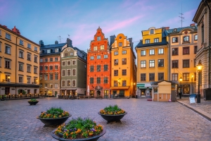 Ein Platz mit historisch bunten Gebäuden und Blumenkübeln bei Sonnenuntergang.