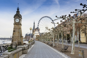 Rheinpromenade in Düsseldorf mit Uhrturm und Riesenrad im Hintergrund.