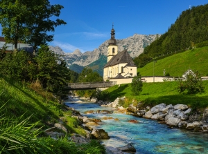 Kirche am Fluss mit Bergen im Hintergrund bei klarem Himmel.