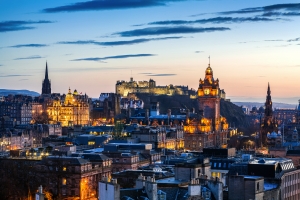 Blick auf Edinburgh zur Dämmerung im Winter, beleuchtete Stadt mit der Burg im Hintergrund.