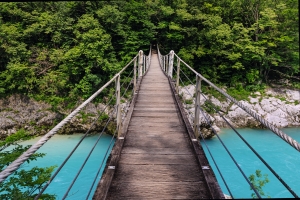Hängebrücke über türkisfarbenem Fluss, umgeben von üppigem Grün.