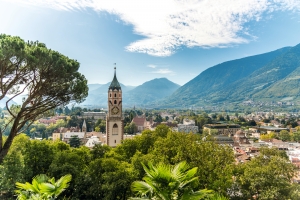 Stadt mit Kirchturm vor einer Bergkulisse an einem klaren Tag.