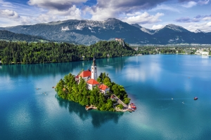 Insel mit Kirche im türkisblauen See, umgeben von Bergen und Wäldern.