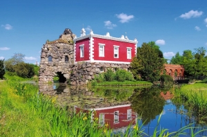 Ein rotes Gebäude mit Steinruine am Teich, umgeben von grüner Vegetation.