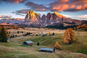 Berglandschaft mit Hütten und herbstlichen Bäumen bei Sonnenuntergang in den Dolomiten.