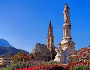 Statue vor einem gotischen Dom mit bunten Blumen im Vordergrund.
