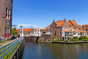 Niederländische Stadtansicht mit historischen Backsteinhäusern, einer Zugbrücke über einen Kanal und blauem Himmel im Hintergrund.