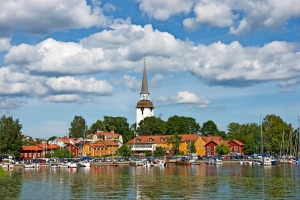 Bunte Häuser und ein Kirchturm am Seeufer unter blauem Himmel mit Wolken.