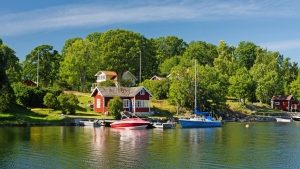 Rotes Haus mit Booten an einem See, umgeben von grünen Bäumen.