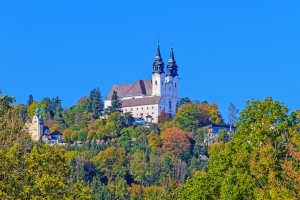 Eine Kirche mit zwei Türmen, umgeben von Bäumen auf einem Hügel bei klarem, blauem Himmel.