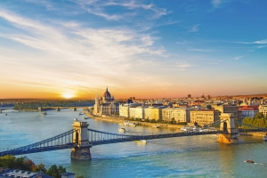 Flussansicht mit Brücke und historischen Gebäuden bei Sonnenuntergang.