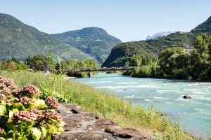 Fluss in einer bergigen Landschaft mit Brücke und grünem Ufer im Vordergrund