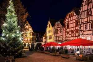 Festlich beleuchteter Platz mit Fachwerkhäusern und Weihnachtsbaum bei Nacht.
