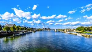 Fluss mit Brücke, Stadtgebäude und blauem Himmel mit Wolken.