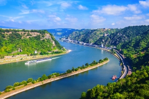 Flusslandschaft mit Hügeln, Bahngleisen und Booten bei sonnigem Wetter