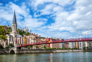 Flussansicht mit einer Kirche, einer roten Brücke und bunten Gebäuden im Hintergrund.