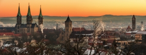 Stadtansicht bei Sonnenaufgang mit historischen Kirchtürmen und Dächern im Winter.