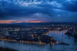 Blick auf Stadt und Fluss bei Dämmerung mit dramatischem Wolkenhimmel.
