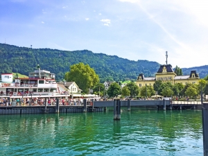 Schiff legt am Hafen an, im Hintergrund ein historisches Gebäude mit Bergen und Wald.