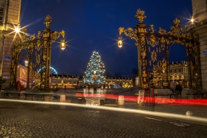 Verzierte Tore bei Nacht mit beleuchtetem Weihnachtsbaum im Hintergrund.