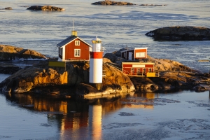 Roter Leuchtturm und Häuser auf felsiger Insel in winterlicher Meereslandschaft.