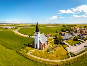 Kirche in grüner Landschaft mit Dorf und klarem Himmel im Hintergrund.