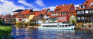 Bunte Fachwerkhäuser an einem Fluss mit einem weißen Touristenboot im Vordergrund.