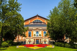Gebäude mit bunter Blumenbeet-Vorderseite, umgeben von Bäumen an einem sonnigen Tag.