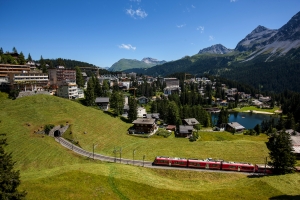 Berglandschaft mit Zug, Gebäuden und See bei sonnigem Wetter in Arosa, Schweiz.