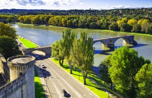 Flusslandschaft mit mittelalterlicher Brücke und Straße mit Autos im Vordergrund
