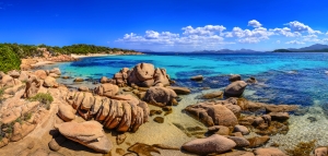 Strand mit Felsen und klarem blauem Wasser unter blauem Himmel.
