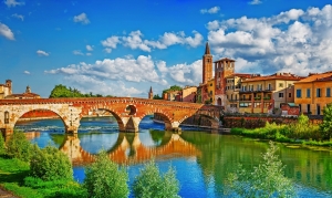 Historische Brücke über Fluss in malerischer Stadt mit Kirchturm und bunten Häusern.