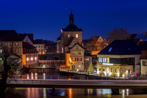 Nächtliche Stadtansicht mit beleuchteten Gebäuden und einer Brücke über einen Fluss.