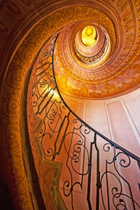 Blick nach oben durch eine verzierte Wendeltreppe mit schmiedeeisernem Geländer.