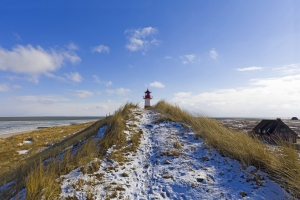Leuchtturm auf einer verschneiten Dünenlandschaft am Meer bei blauem Himmel.